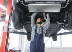 Mechanikas autoservise tikrina keltuvu pakelto automobilio apačią