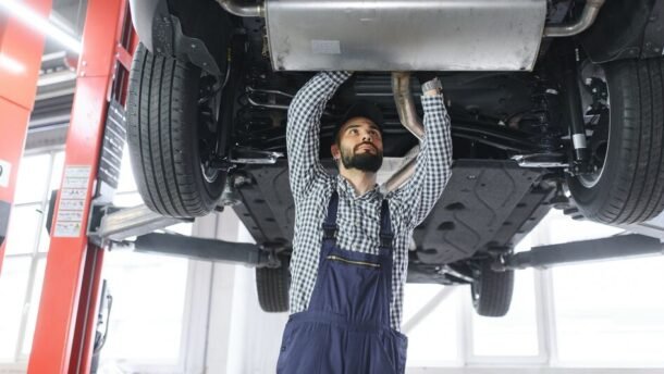 Mechanikas autoservise tikrina keltuvu pakelto automobilio apačią