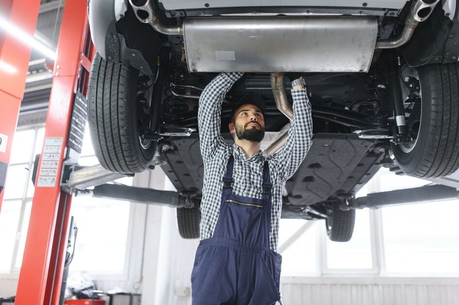 Mechanikas autoservise tikrina keltuvu pakelto automobilio apačią