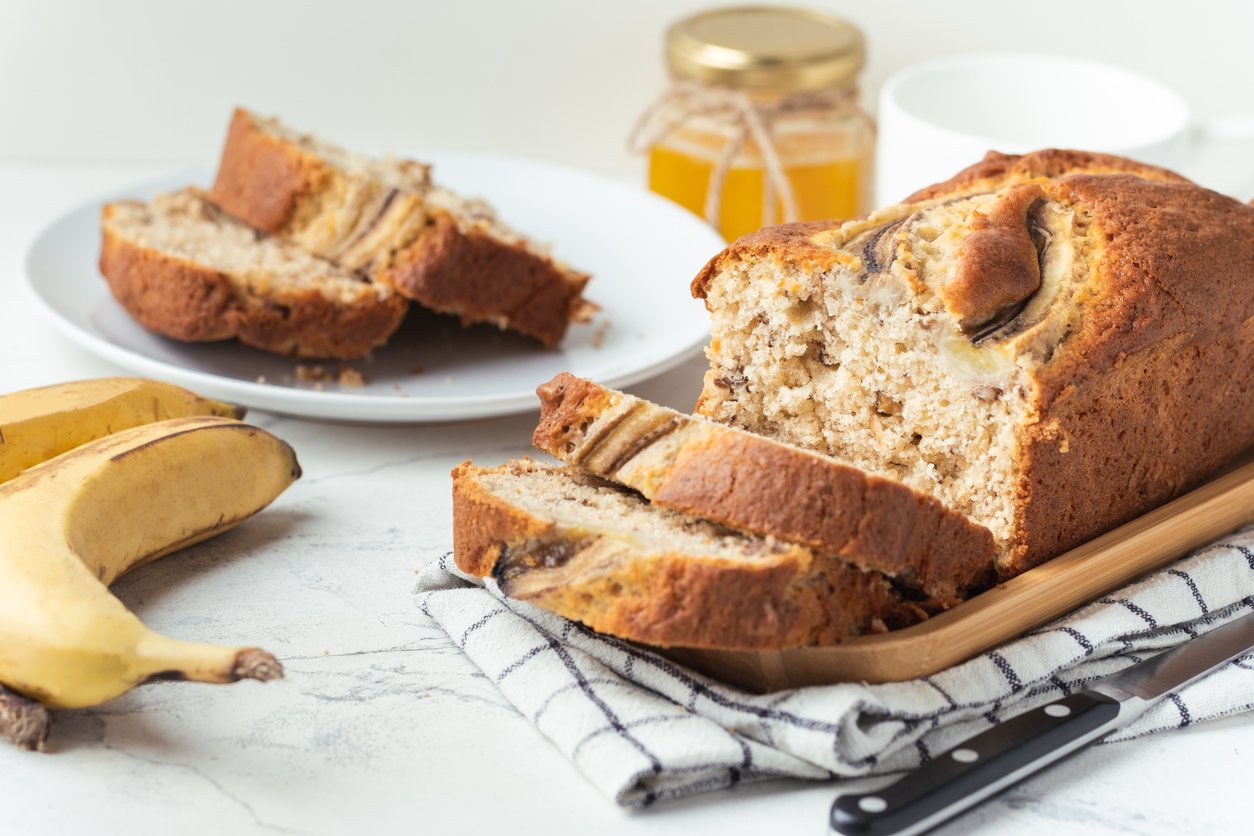 Riekelėmis supjaustytas bananų kepalas ant medinės lentelės, šalia bananai ir peilis