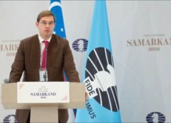 Vyras kalba prie tribūnos FIDE kongrese Samarkande