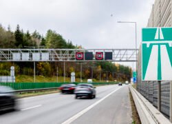Greitkelyje važiuojantys automobiliai ir virš kelio rodomi 130 km/h ženklai