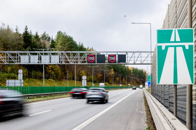 Greitkelyje važiuojantys automobiliai ir virš kelio rodomi 130 km/h ženklai