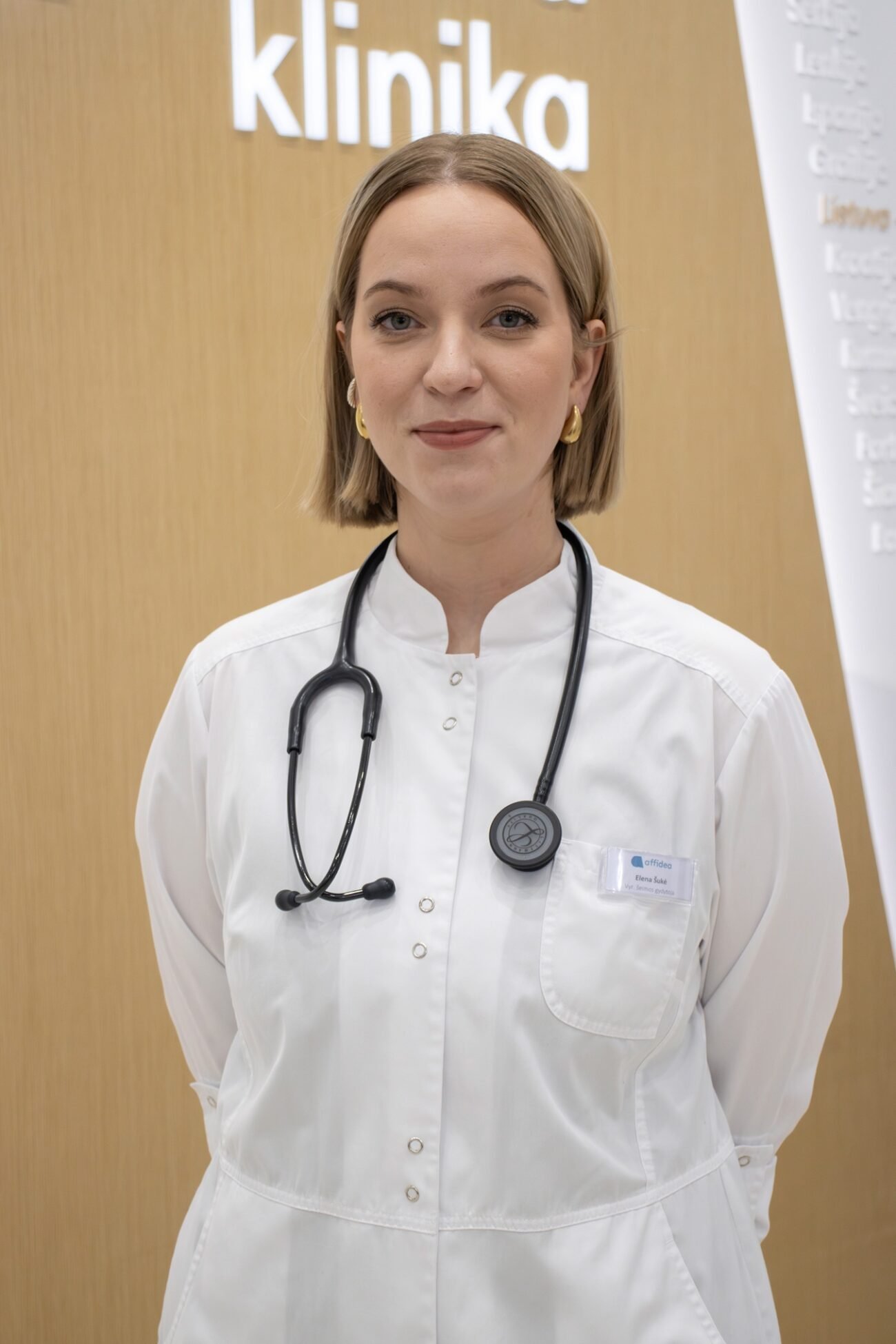 Gydytoja baltais chalatais su stetoskopu klinikos aplinkoje