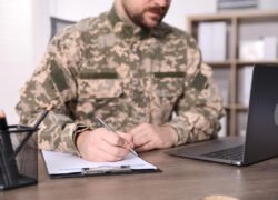 Kareivis maskuojamąja uniforma pildo dokumentą prie nešiojamojo kompiuterio
