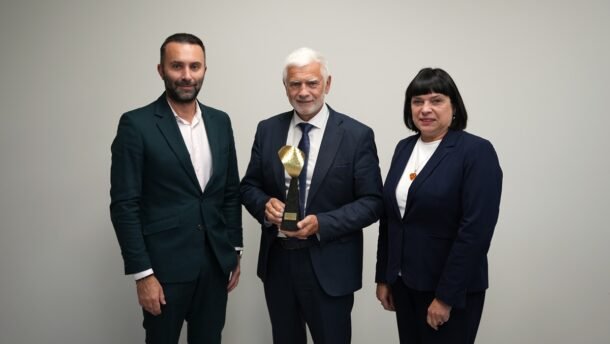 Trys oficialiai apsirengę žmonės pozuoja, o viduryje vyras laiko apdovanojimą