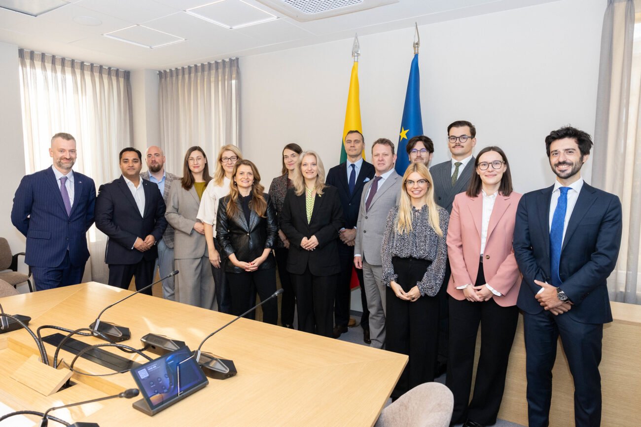 Grupė žmonių posėdžių salėje prie Lietuvos ir Europos Sąjungos vėliavų