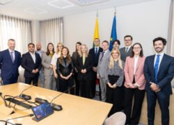 Grupė žmonių posėdžių salėje prie Lietuvos ir Europos Sąjungos vėliavų