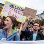 Mokiniai protestuoja su plakatais ir Vokietijos vėliava miesto gatvėje