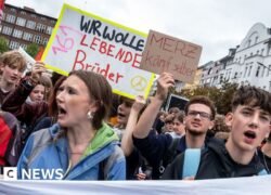 Mokiniai protestuoja su plakatais ir Vokietijos vėliava miesto gatvėje