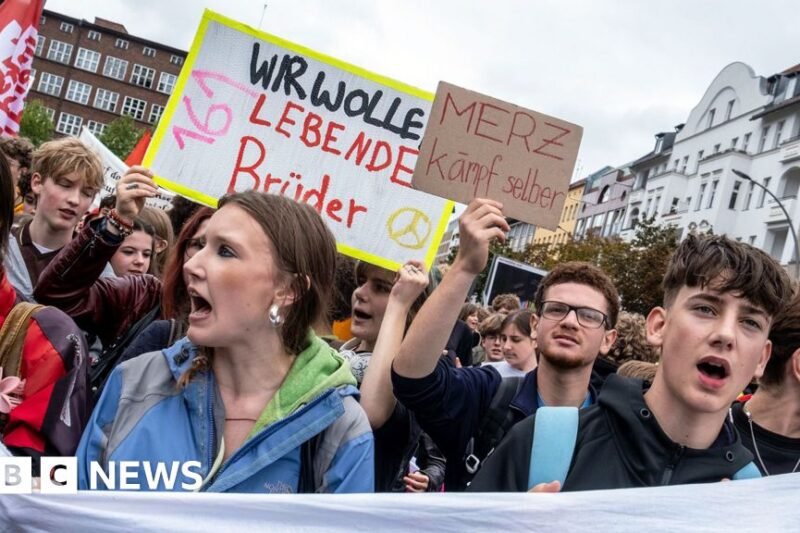 Mokiniai protestuoja su plakatais ir Vokietijos vėliava miesto gatvėje
