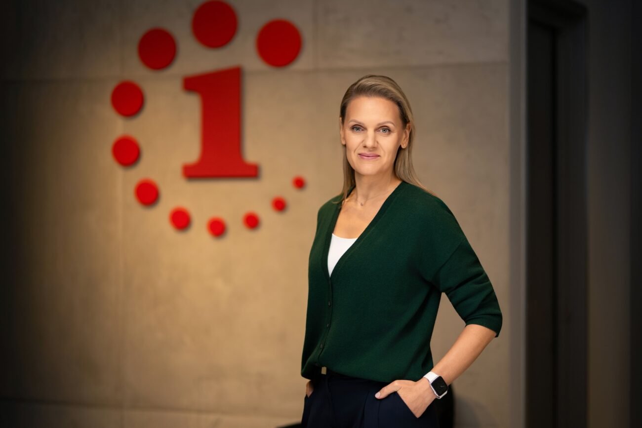 Moteris žalia palaidine stovi prie sienos su raudonu ženklu