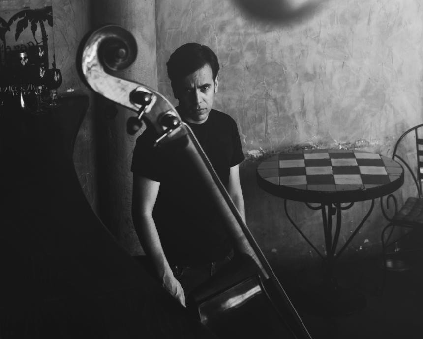 Juodai baltame kadre muzikantas laiko kontrabosą prie languoto staliuko
