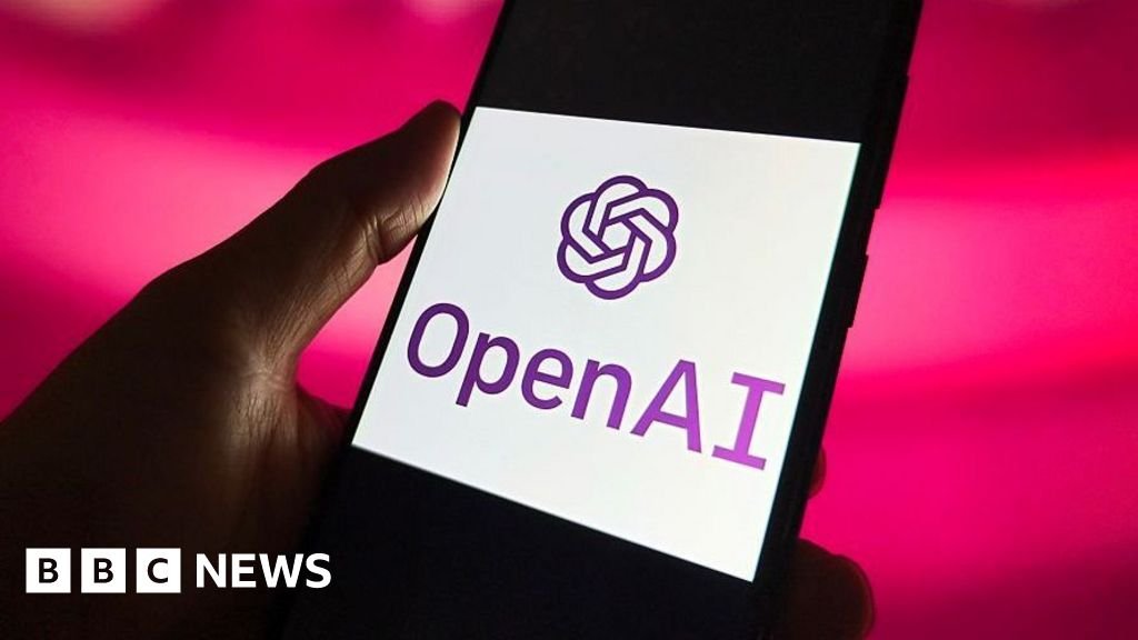 Rankoje laikomas išmanusis telefonas su ekrane rodomu OpenAI logotipu ir pavadinimu