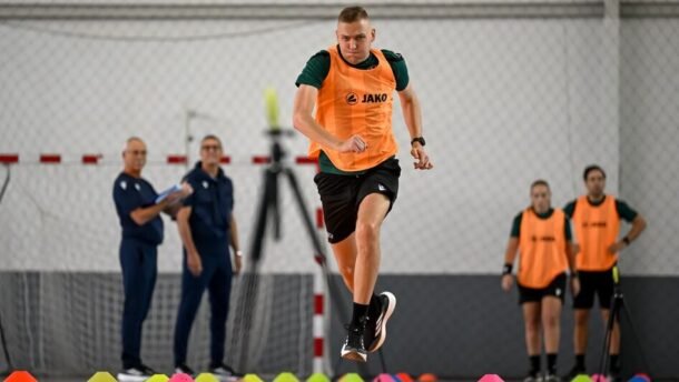 Oranžine liemene vilkintis dalyvis atlieka greičio pratimą salės aikštėje