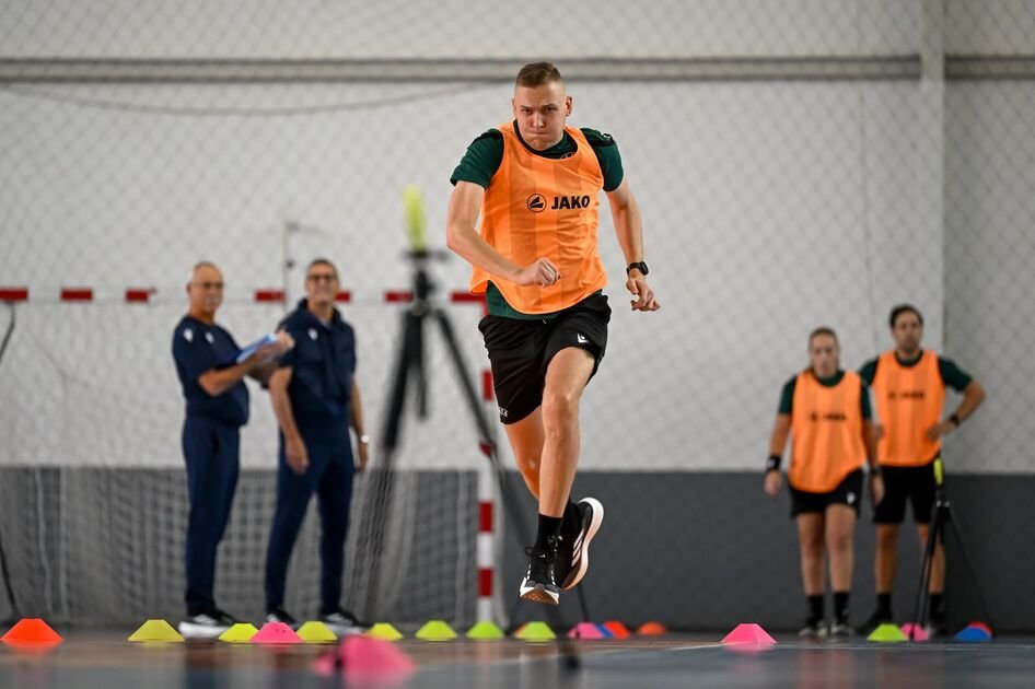 Oranžine liemene vilkintis dalyvis atlieka greičio pratimą salės aikštėje