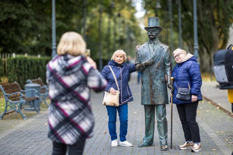 Dvi senjorės pozuoja šalia vyro skulptūros Palangos parke