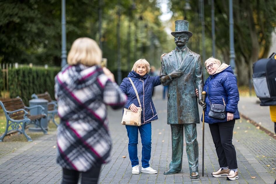 Dvi senjorės pozuoja šalia vyro skulptūros Palangos parke