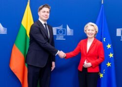 Du žmonės spaudžia rankas Europos Komisijos ženklu pažymėtame fone