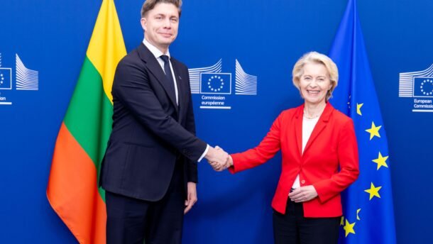 Du žmonės spaudžia rankas Europos Komisijos ženklu pažymėtame fone