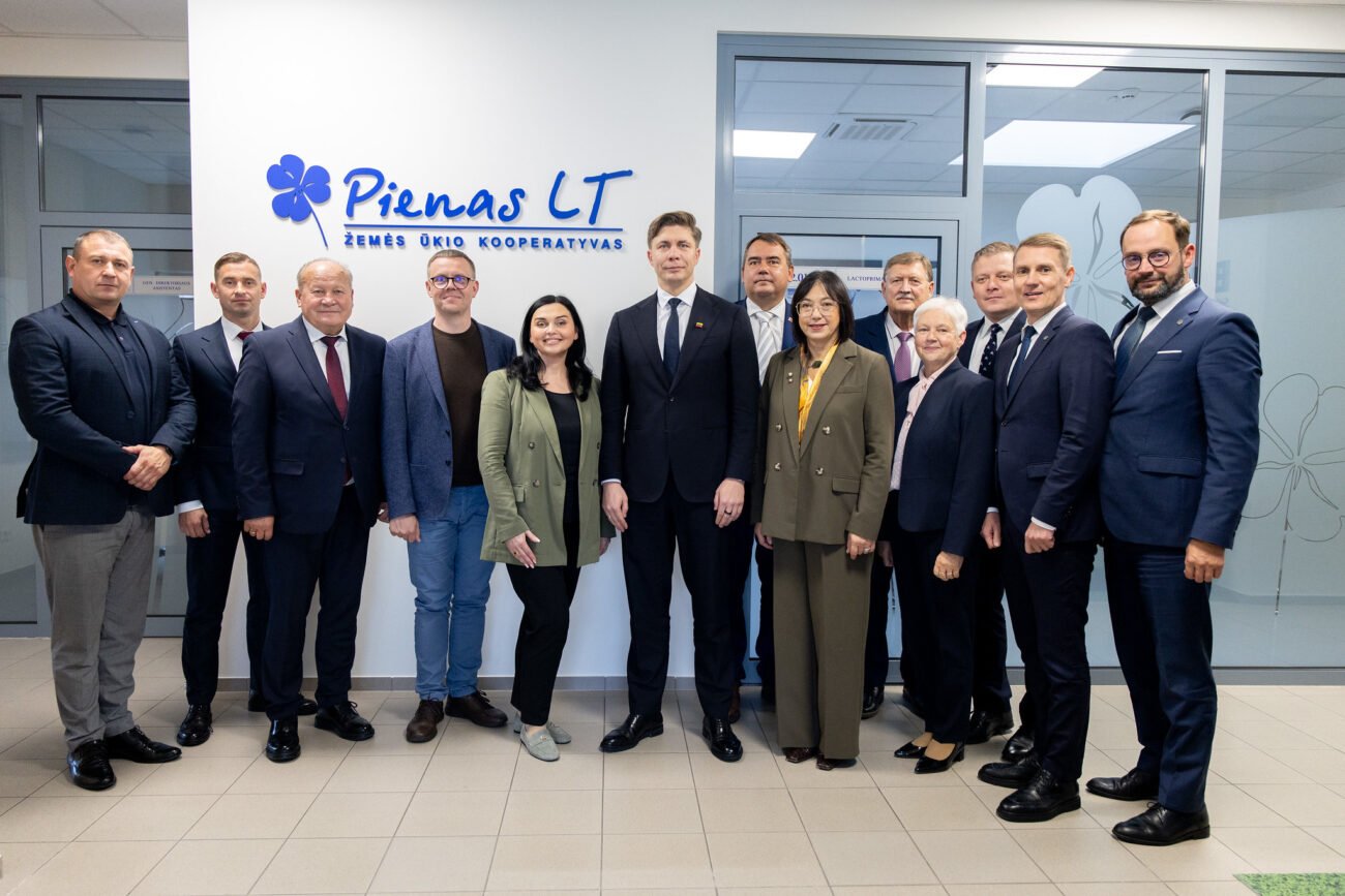 Žmonių grupė stovi prie „Pienas LT“ įmonės logotipo