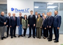 Žmonių grupė stovi prie „Pienas LT“ įmonės logotipo