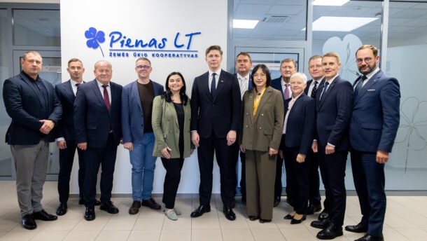 Žmonių grupė stovi prie „Pienas LT“ įmonės logotipo