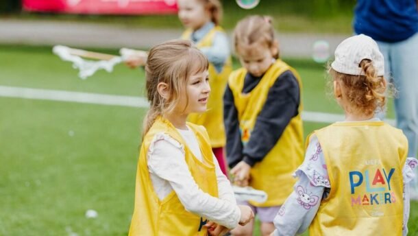 Vaikai geltonomis liemenėmis žaidžia futbolo aikštėje