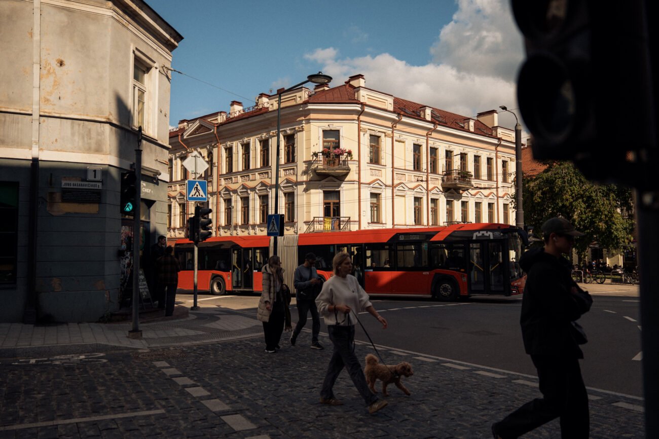 Vilniaus gatvėje praeiviai eina šalia raudonų miesto autobusų
