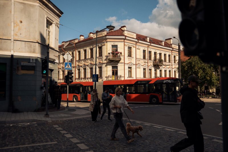 Vilniaus gatvėje praeiviai eina šalia raudonų miesto autobusų