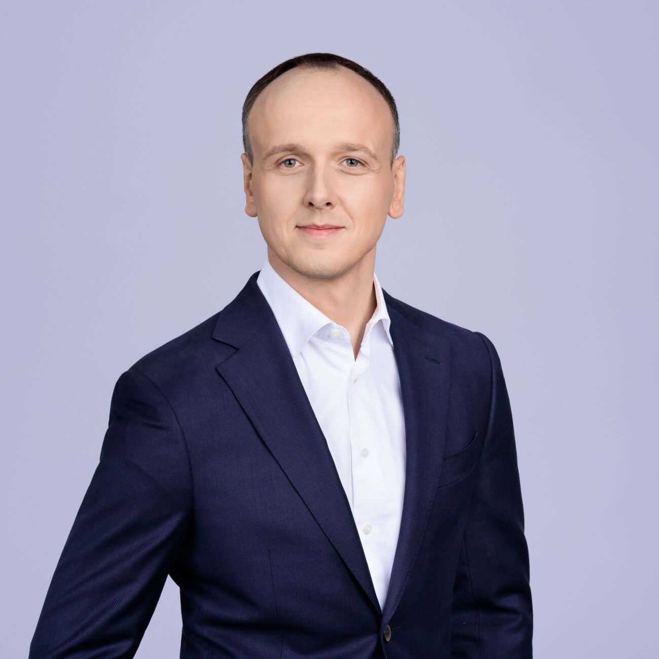 Vyras su tamsiai mėlynu kostiumu ir baltais marškiniais šviesiame fone