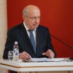 Andrius Kubilius sėdi prie tribūnos su dokumentais ir mikrofonu