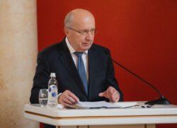Andrius Kubilius sėdi prie tribūnos su dokumentais ir mikrofonu