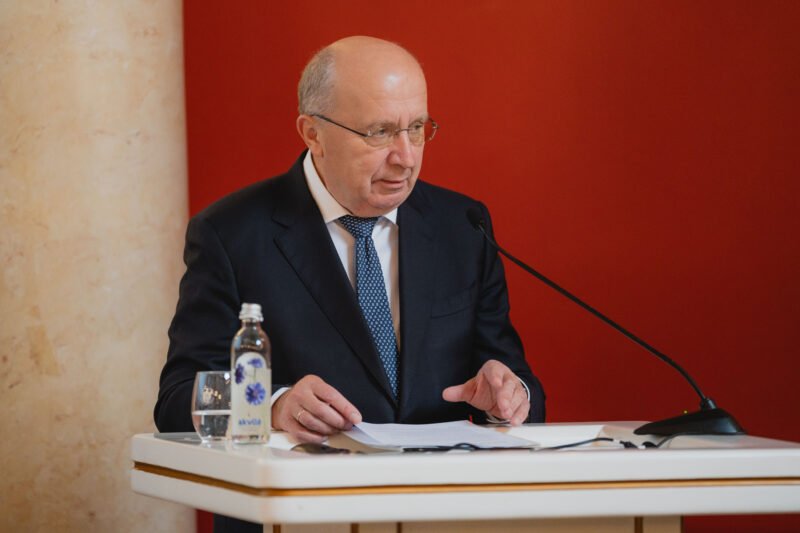 Andrius Kubilius sėdi prie tribūnos su dokumentais ir mikrofonu