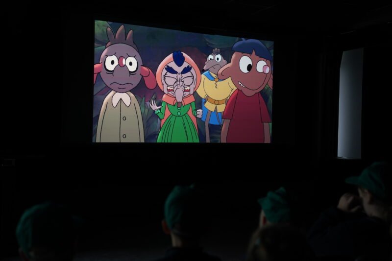 Kino salėje rodomas animacinis filmas, o pirmame plane matyti žiūrovų siluetai