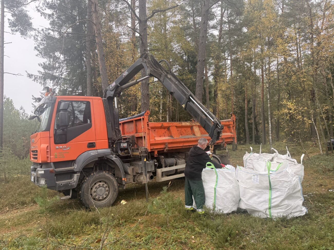 Miške prie oranžinio sunkvežimio sukrauti didmaišiai su atliekomis