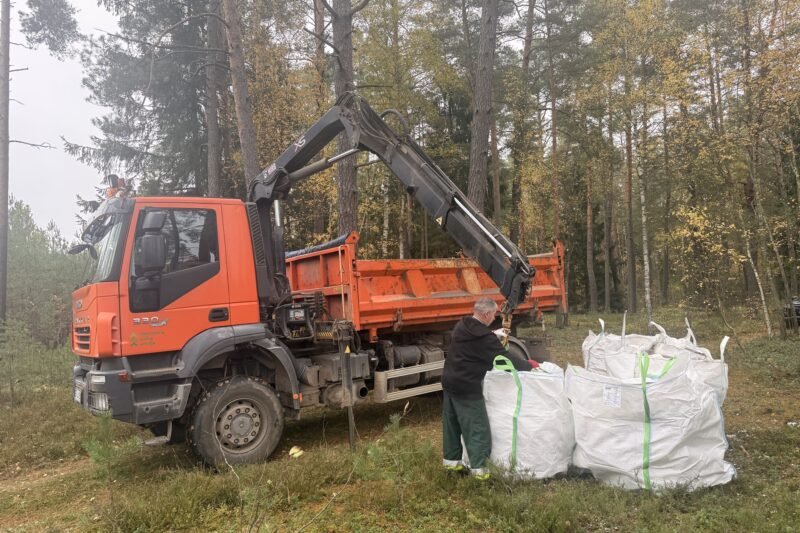 Miške prie oranžinio sunkvežimio sukrauti didmaišiai su atliekomis