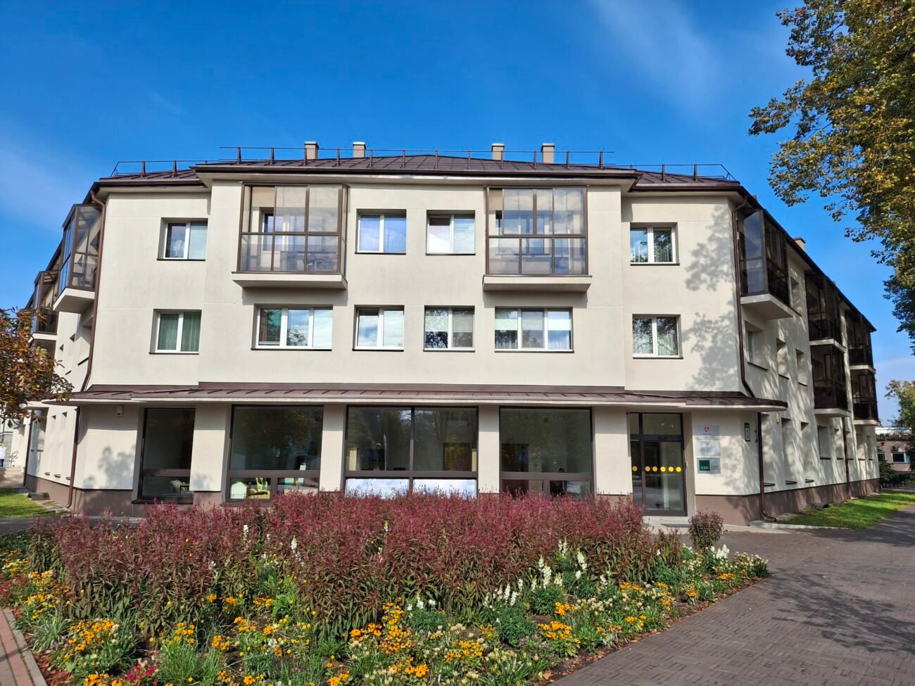 Atnaujintas daugiabutis pastatas su gėlynu ir medžiais priekyje