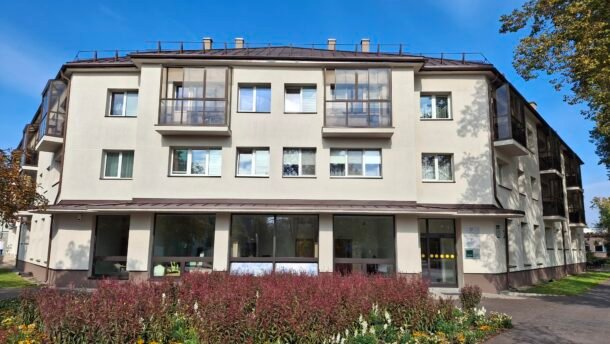 Atnaujintas daugiabutis pastatas su gėlynu ir medžiais priekyje