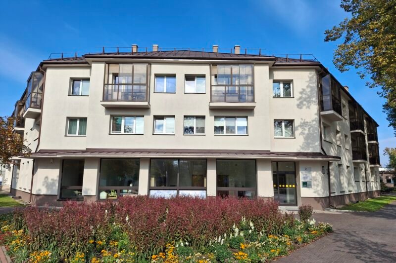 Atnaujintas daugiabutis pastatas su gėlynu ir medžiais priekyje