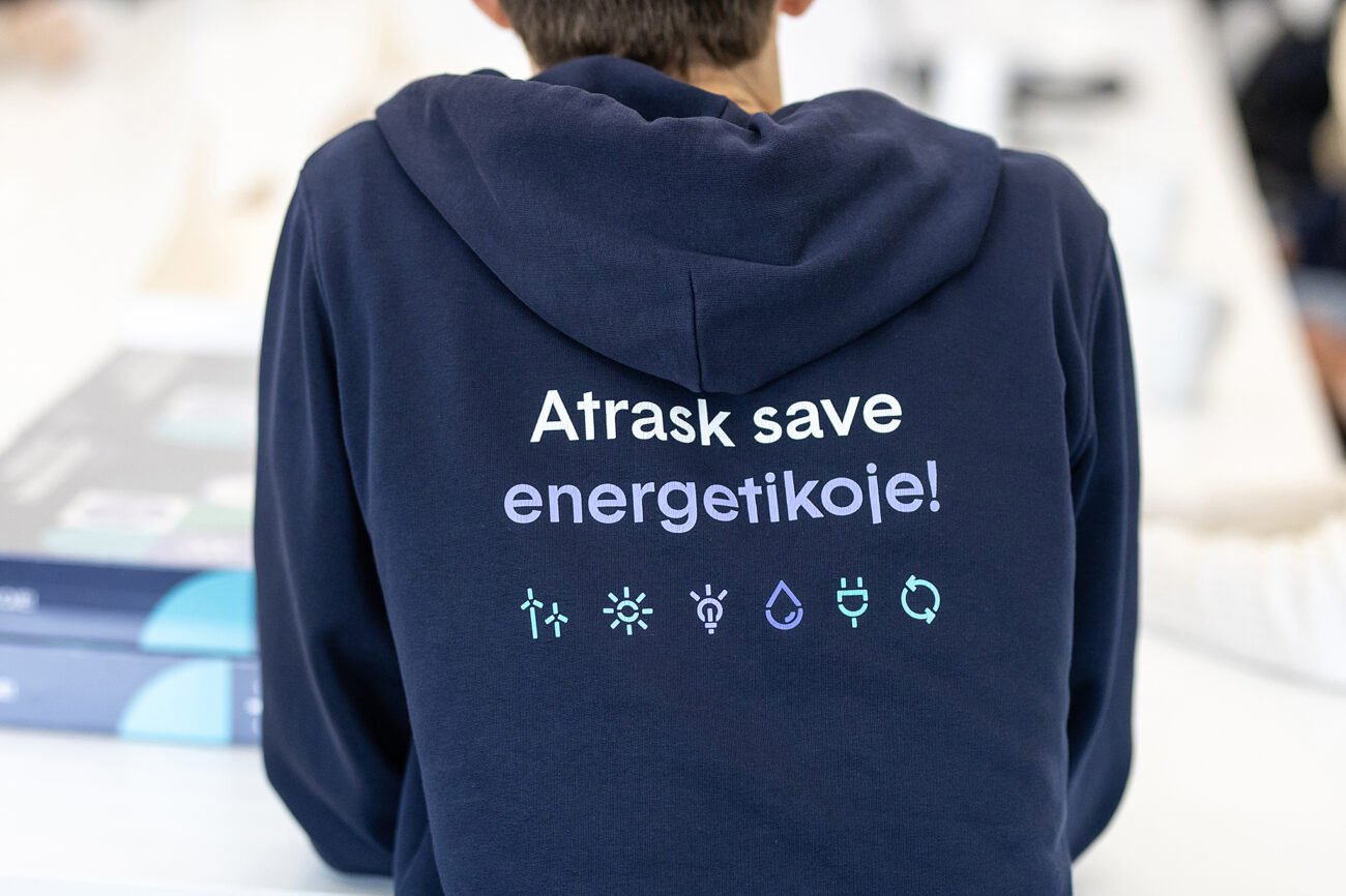 Asmuo su tamsiai mėlynu džemperiu ir užrašu „Atrask save energetikoje!“