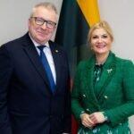 Oficialiai apsirengęs vyras ir moteris pozuoja šalia vėliavų