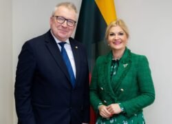 Oficialiai apsirengęs vyras ir moteris pozuoja šalia vėliavų