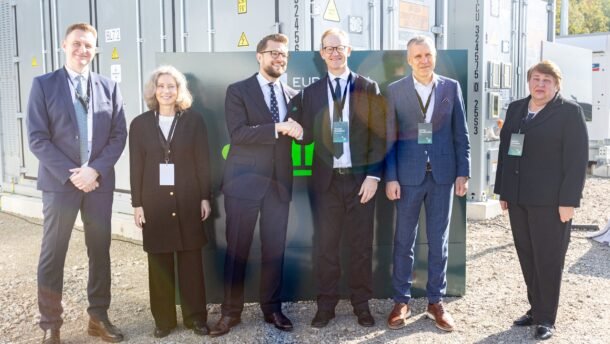 Šeši žmonės stovi priešais baterijų energijos kaupimo įrenginių konteinerius