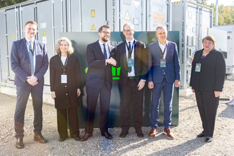 Šeši žmonės stovi priešais baterijų energijos kaupimo įrenginių konteinerius