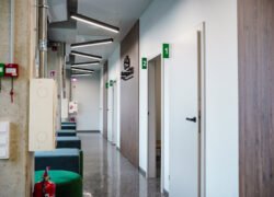 Šviesus klinikos koridorius su numeruotomis durimis, laukimo vietomis ir gesintuvu