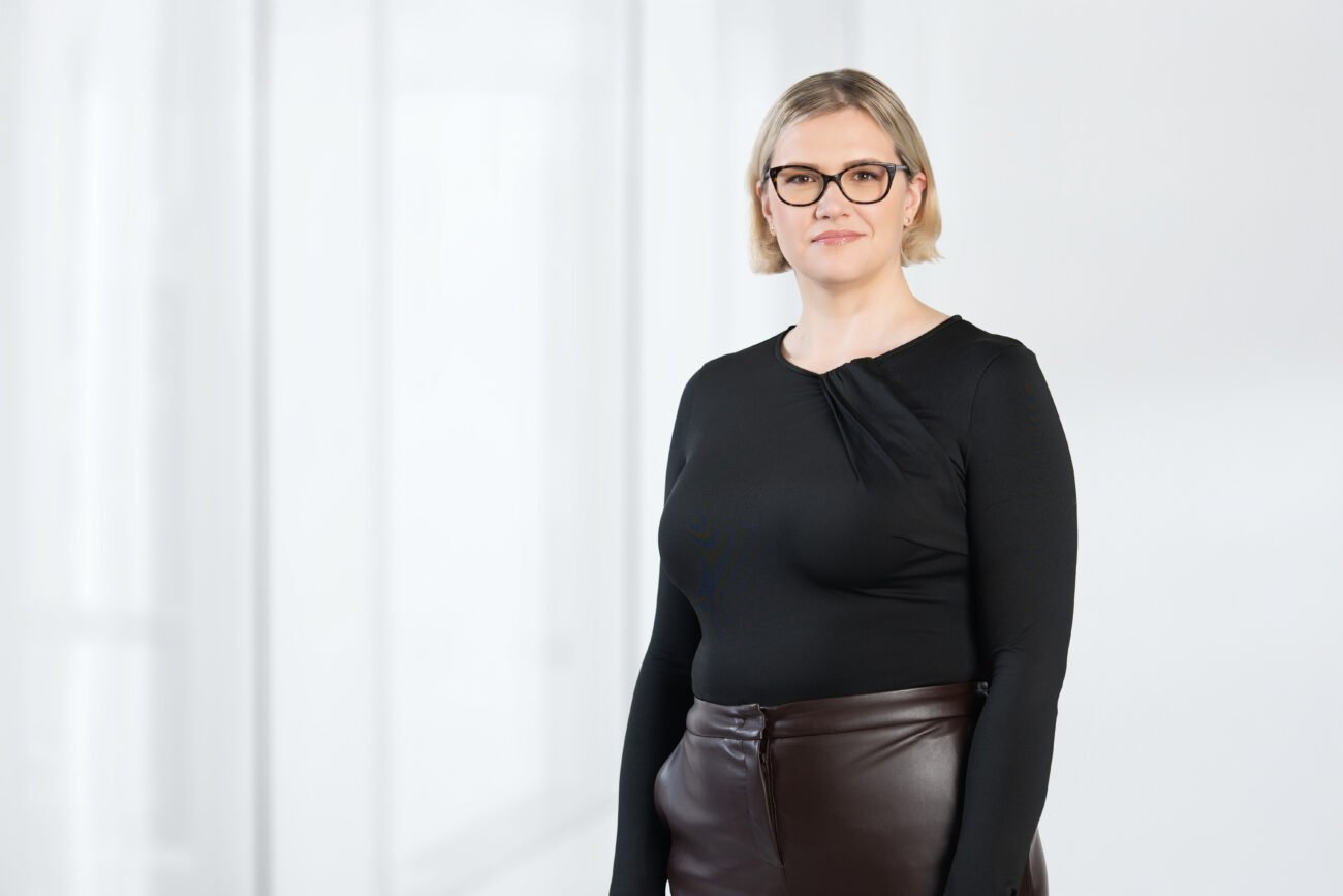 Dalykinis moters portretas su akiniais, vilkinčios juodą palaidinę ir tamsų sijoną