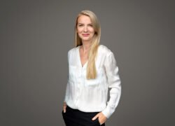 Besijuokianti šviesiaplaukė moteris balta palaidine ir juodomis kelnėmis