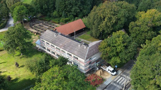 Iš viršaus matomas medžių apsuptas mokyklos pastatas prie kelio