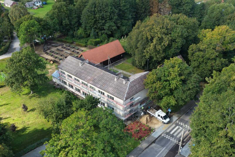 Iš viršaus matomas medžių apsuptas mokyklos pastatas prie kelio